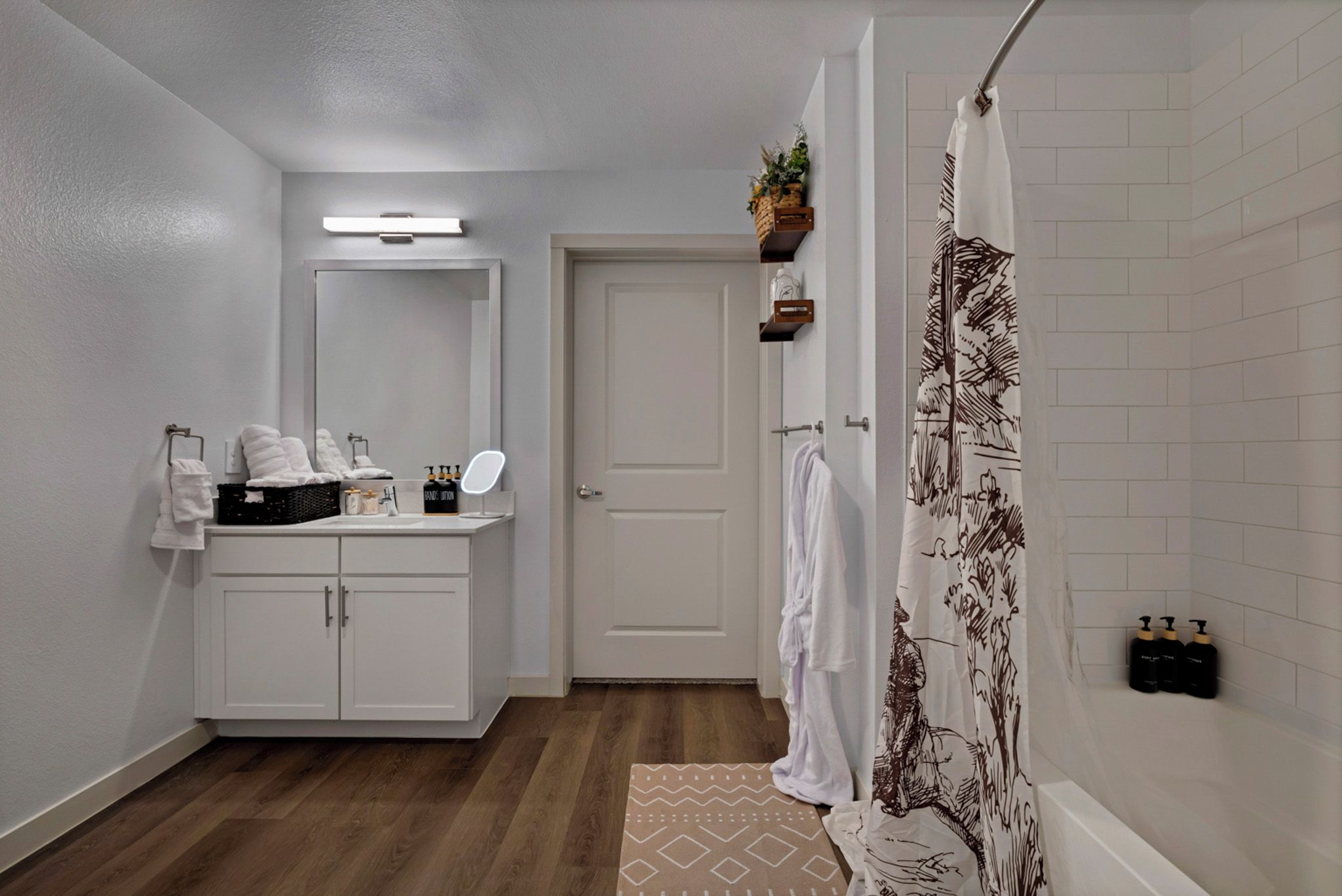 A bathroom with a white vanity, a mirror, a shower curtain with a tree pattern, and a door leading to another room.