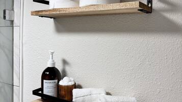 A bathroom with two wooden shelves mounted on the wall, holding toiletries and towels.