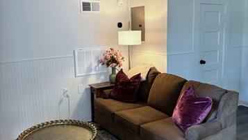 A room with a brown sofa, a round table, a lamp, and a door.