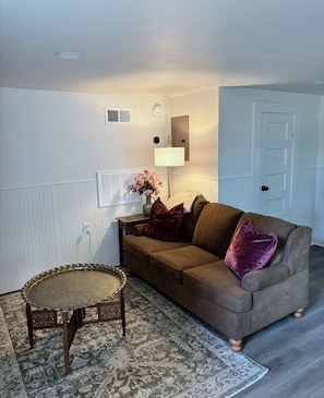 A room with a brown sofa, a round table, a lamp, and a door.