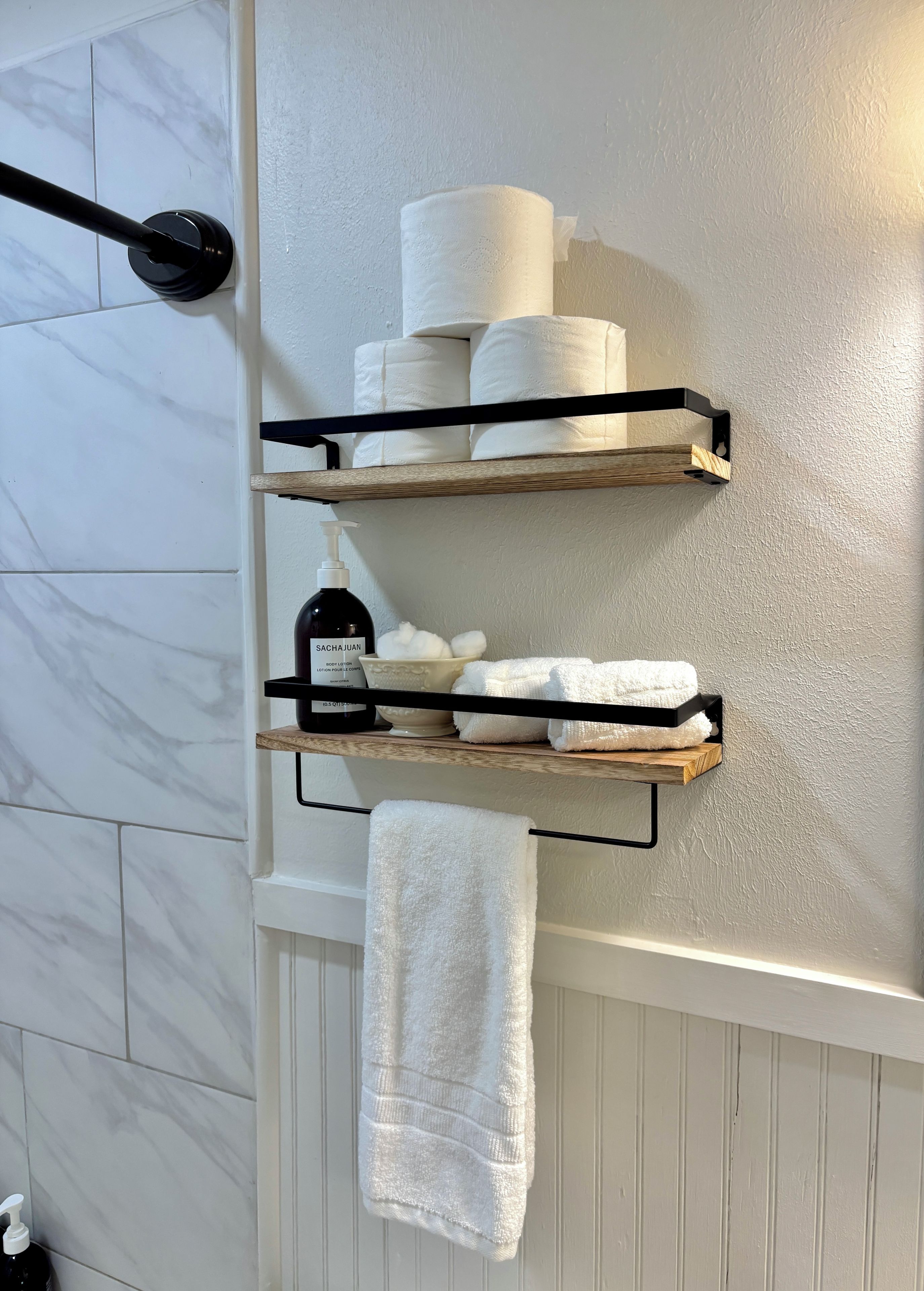 Ein Badezimmer mit Handtuchhalter, einem weißen Handtuch, Ablage für Pflegeprodukte und einer Wand mit Marmorfliesen.
