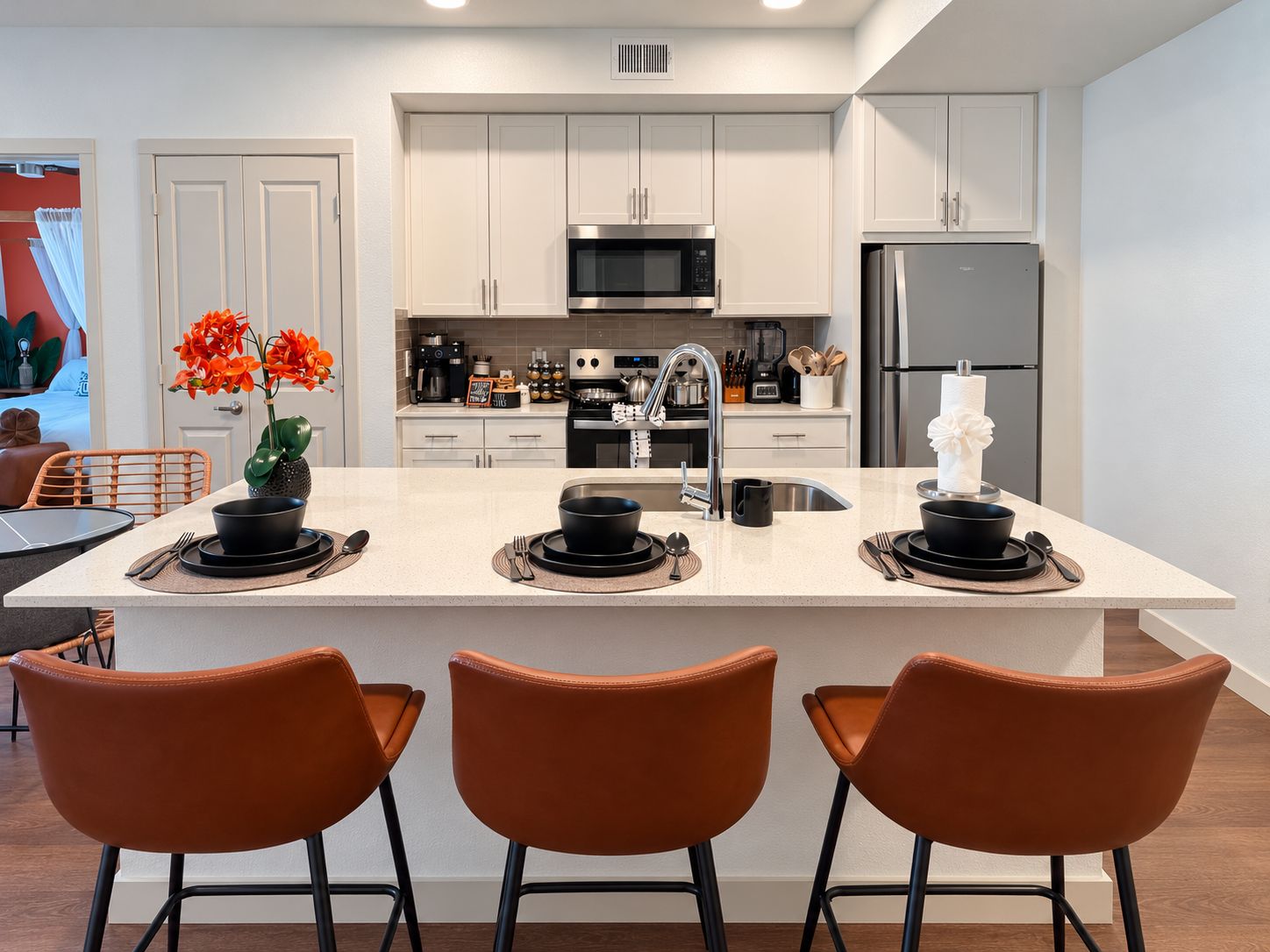 A modern kitchen with white cabinetry, a central island with black cookware, and a stainless steel refrigerator.
