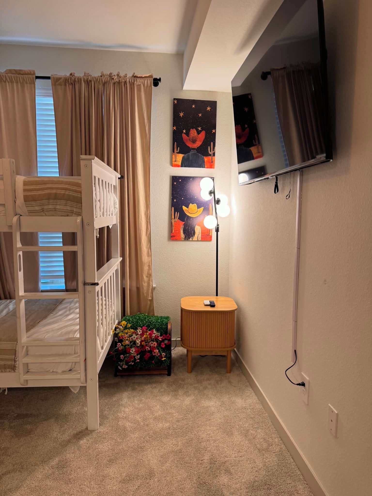 A child's bunk bed, a small round table with a lamp, and wall art.