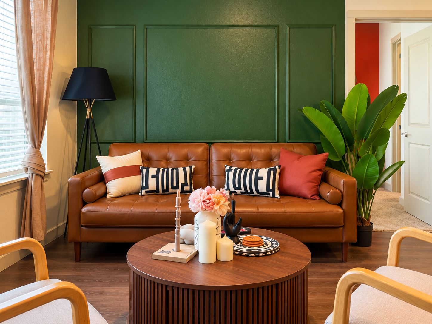 A brown leather sofa with decorative pillows, a round wooden coffee table with a vase and candles, and a large green plant.