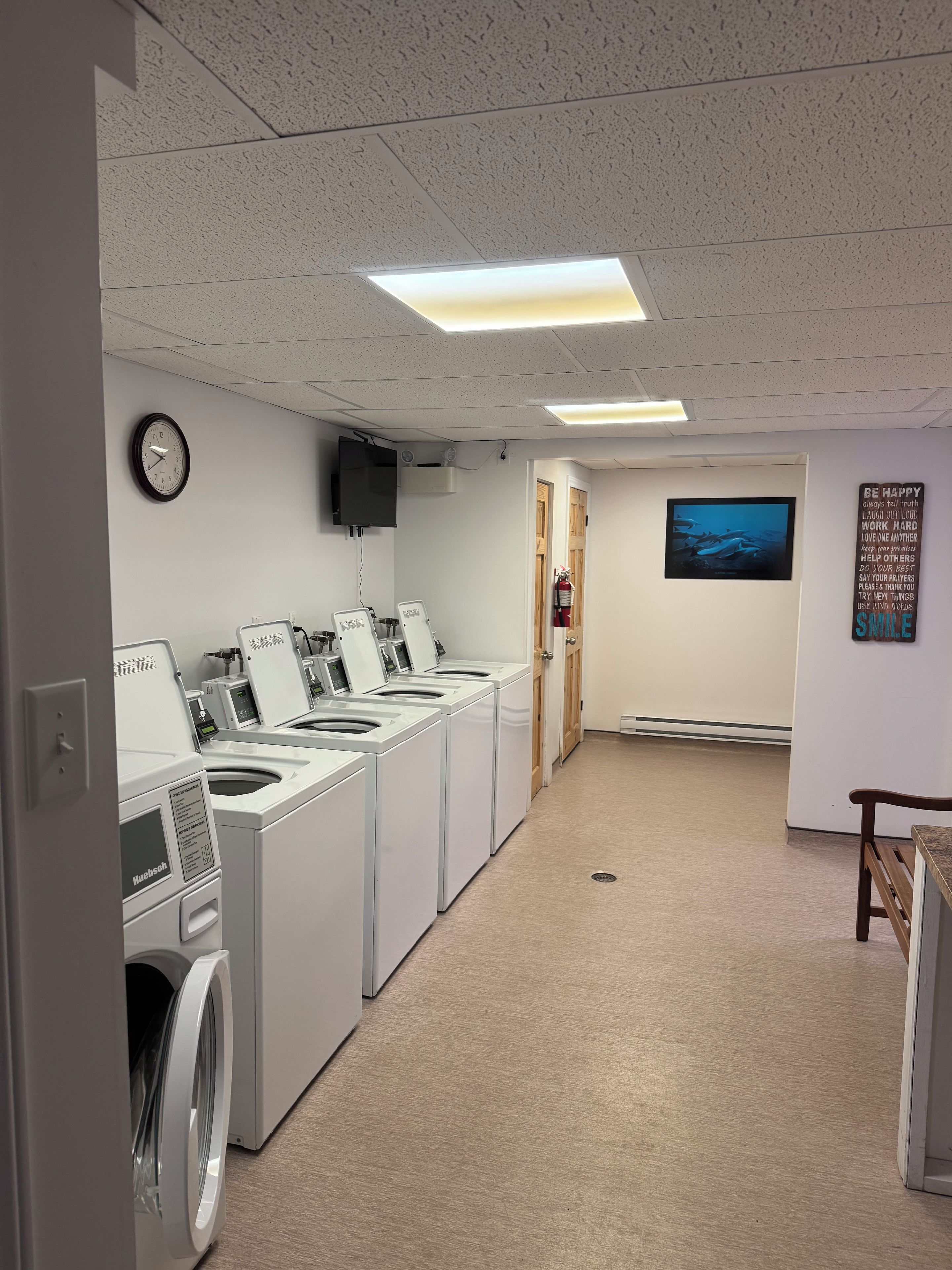 Een wasserette met meerdere wasmachines, een klok, een televisie en een motiverende poster aan de muur.