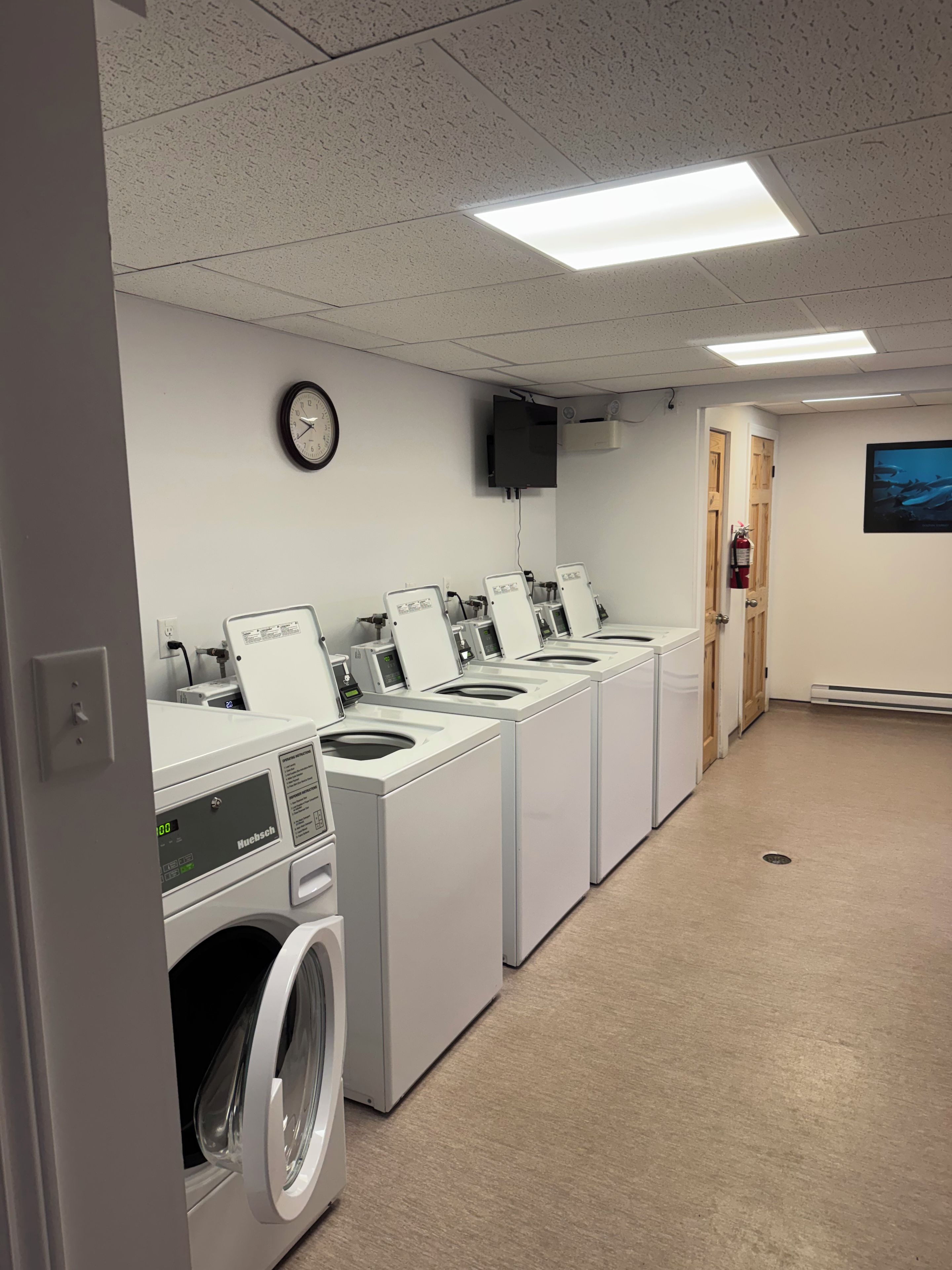 A laundry facility with multiple washing machines, a clock, a television, and a fire extinguisher.
