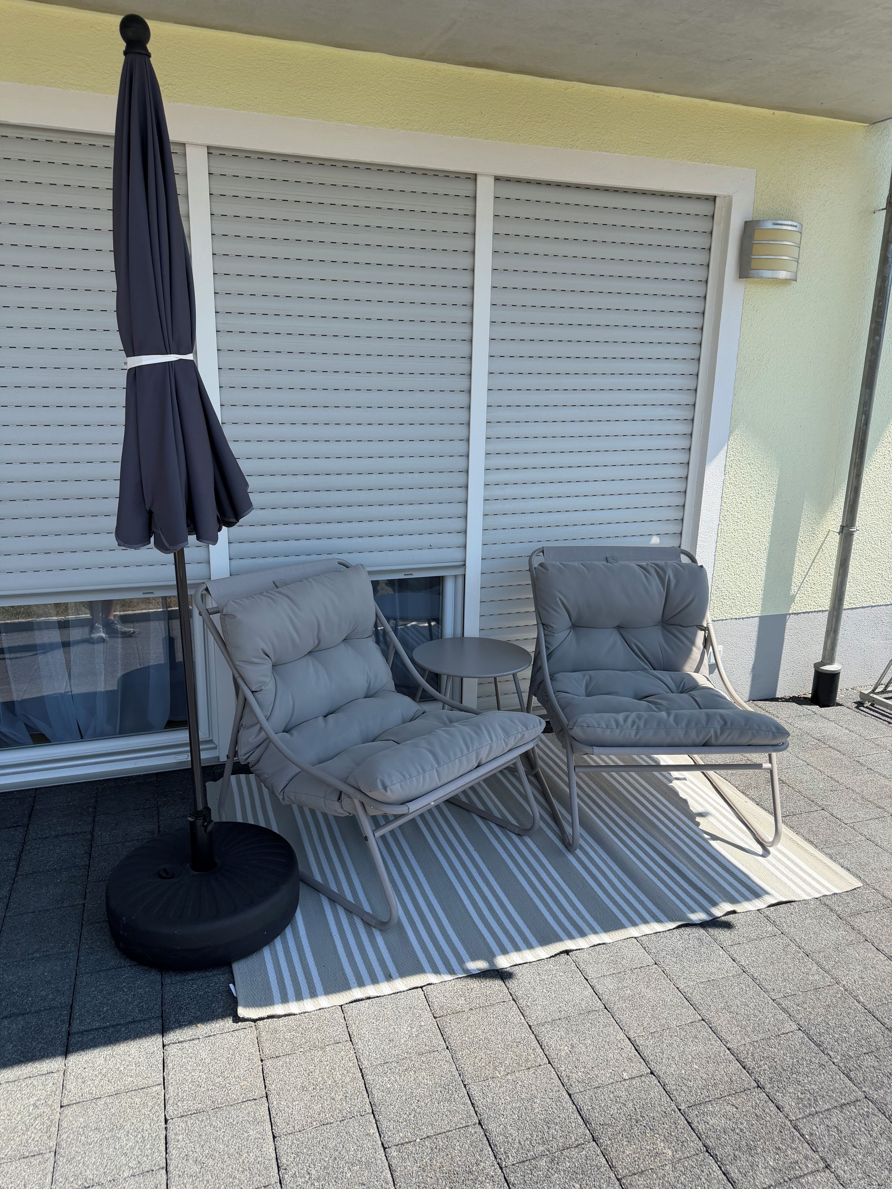 An outdoor seating area with a patio table, two cushioned chairs, a striped rug, and a floor lamp.