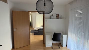 A modern bedroom with a wooden door, a desk with a chair, a bed with a gray blanket, and a hanging light fixture.