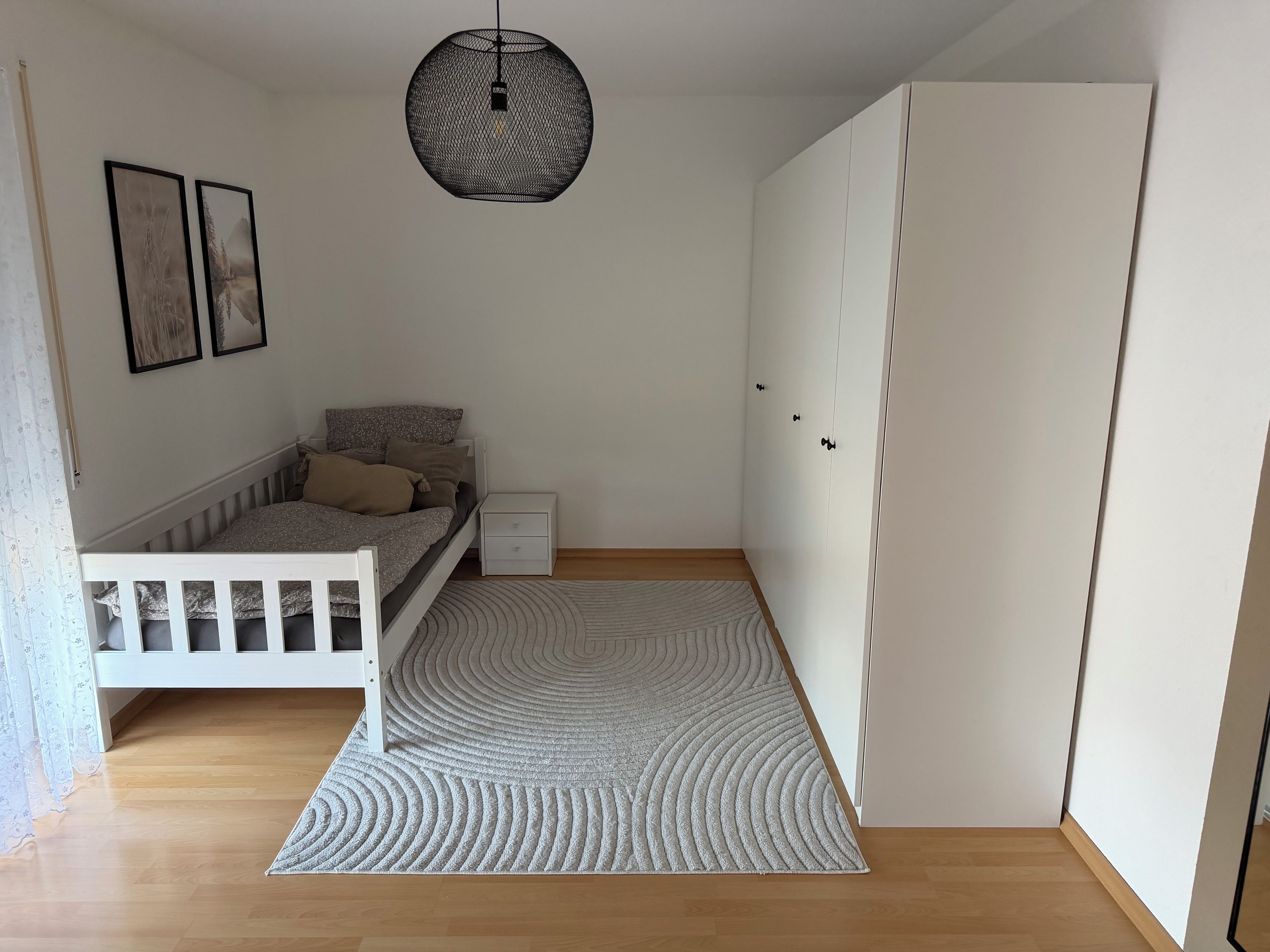 Ein Schlafzimmer mit Bett, Nachttisch, Kleiderschrank und einer Pendelleuchte.