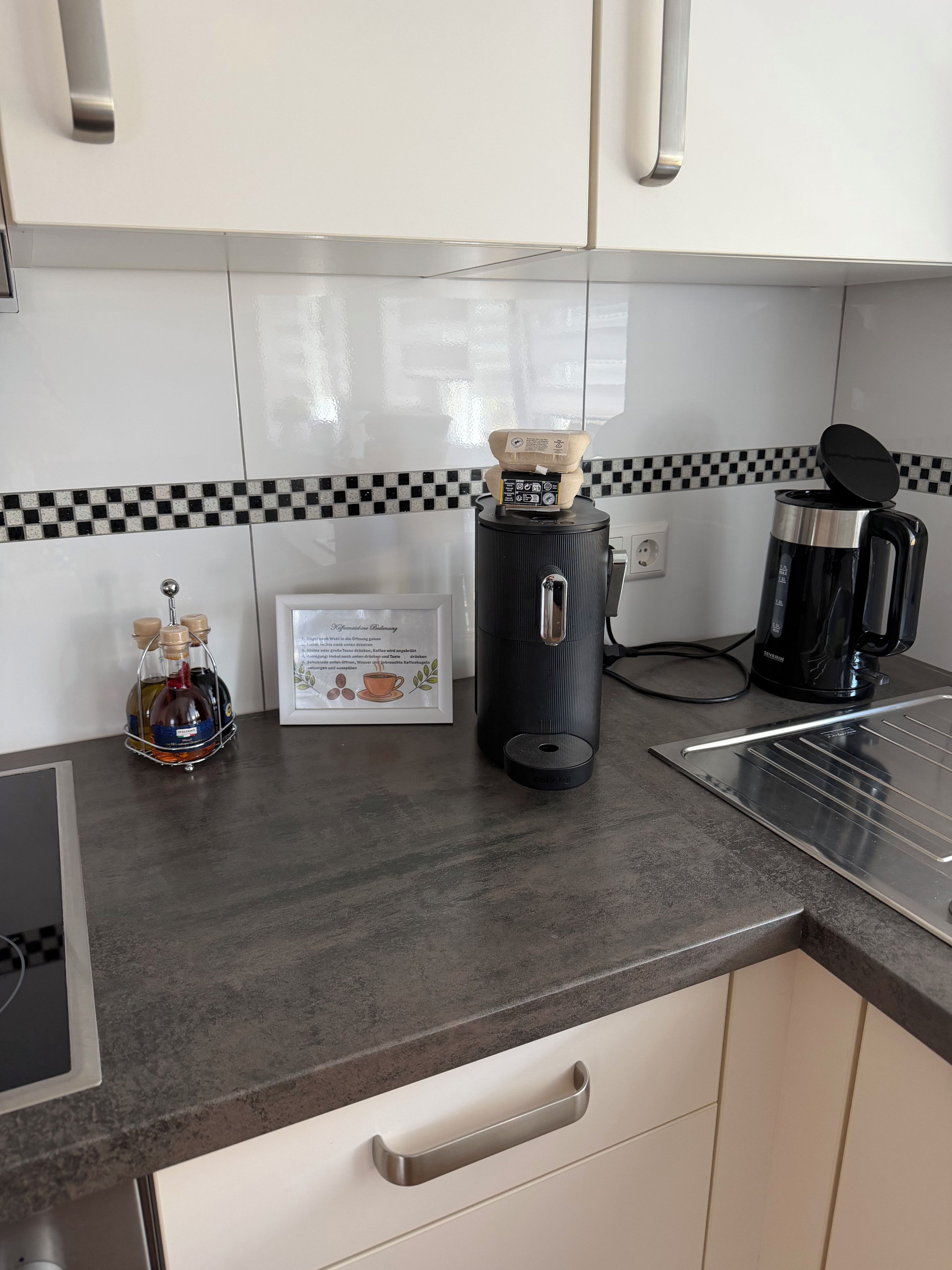 A kitchen with a coffee maker, a kettle, and a bottle of liquor on the counter.