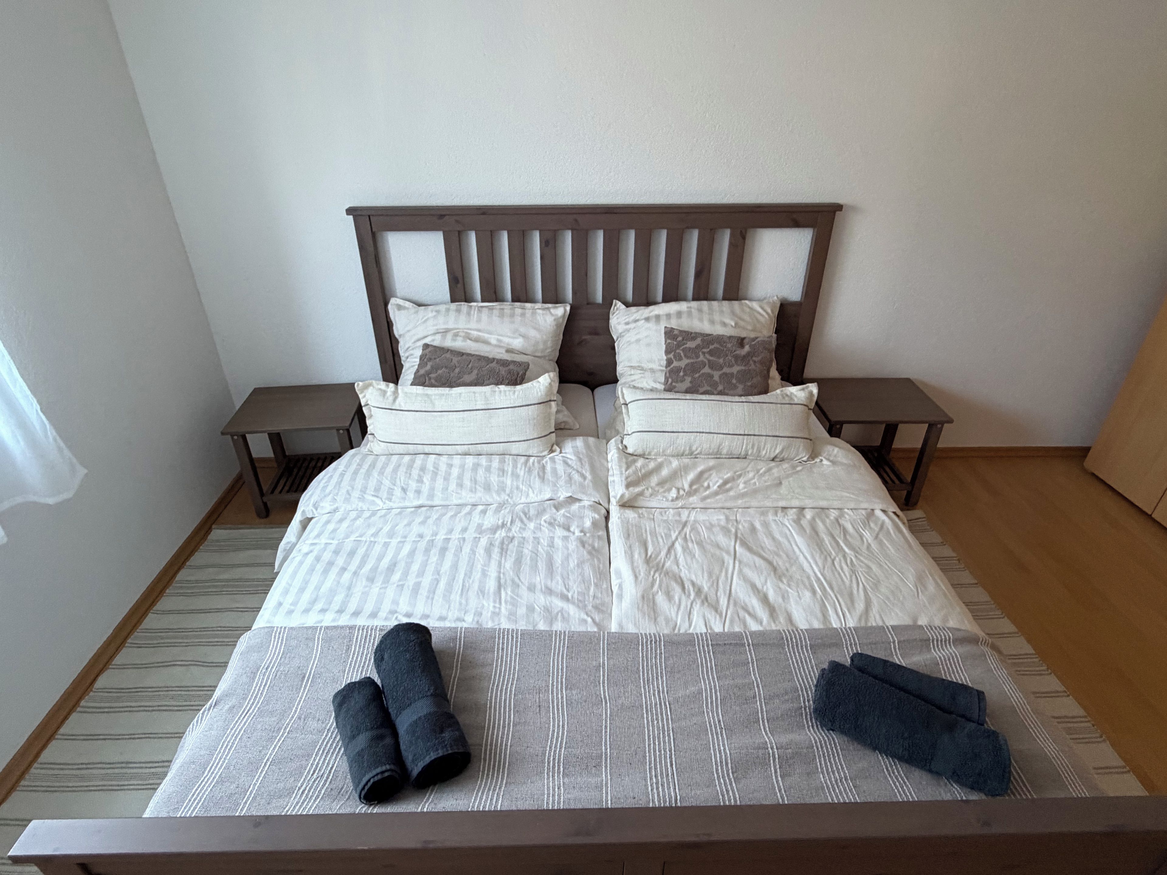 A neatly made bed with a striped bedspread, two pillows, and two rolled towels on the bed.