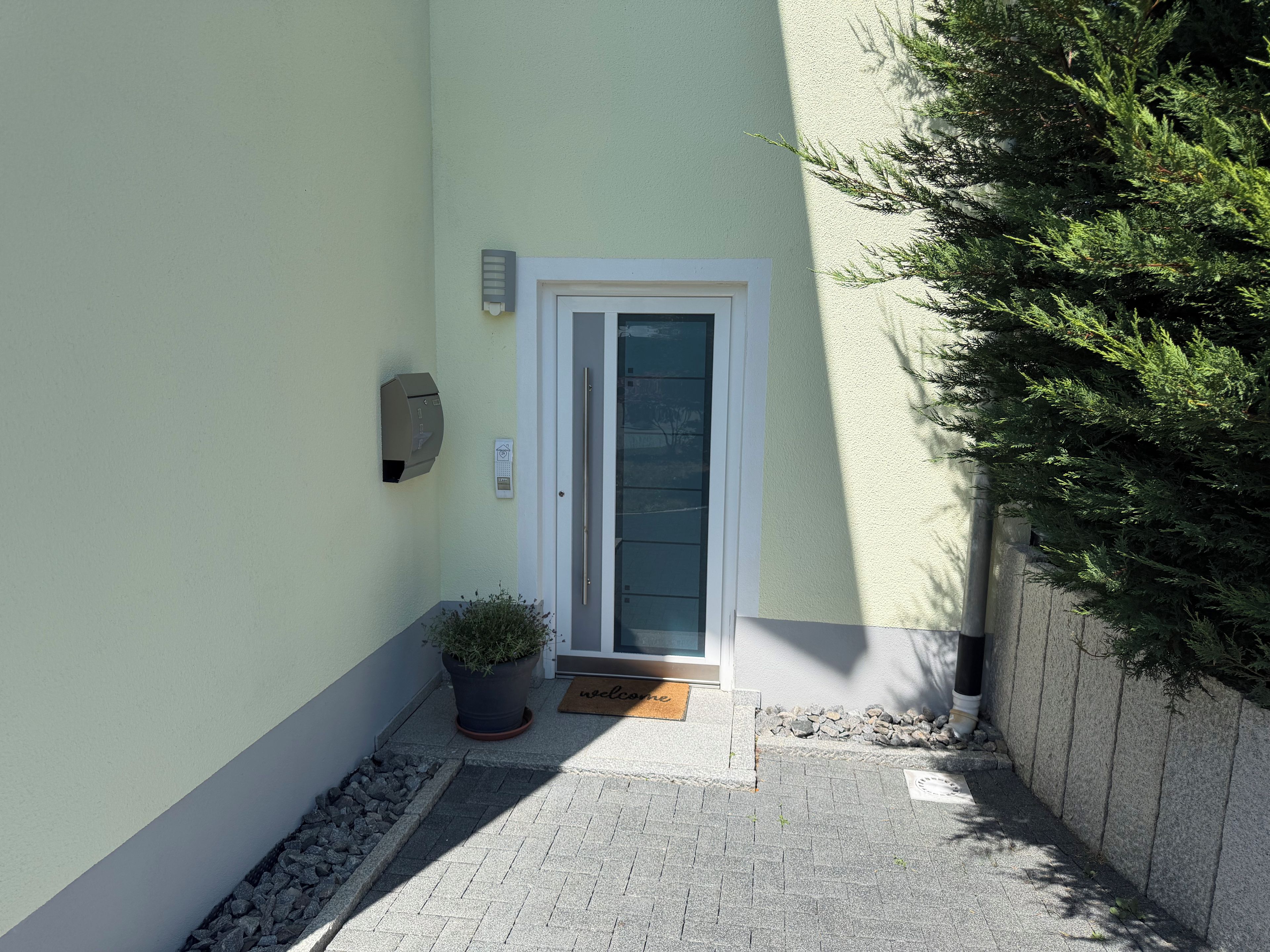 Une petite entrée avec une porte, une boîte aux lettres, un pot de fleurs et un paillasson.