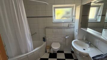Ein Badezimmer mit Badewanne, Toilette, Waschbecken und einem Fenster.