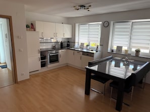 A modern kitchen with white cabinets, a built-in oven, and a dining area with a glass table.
