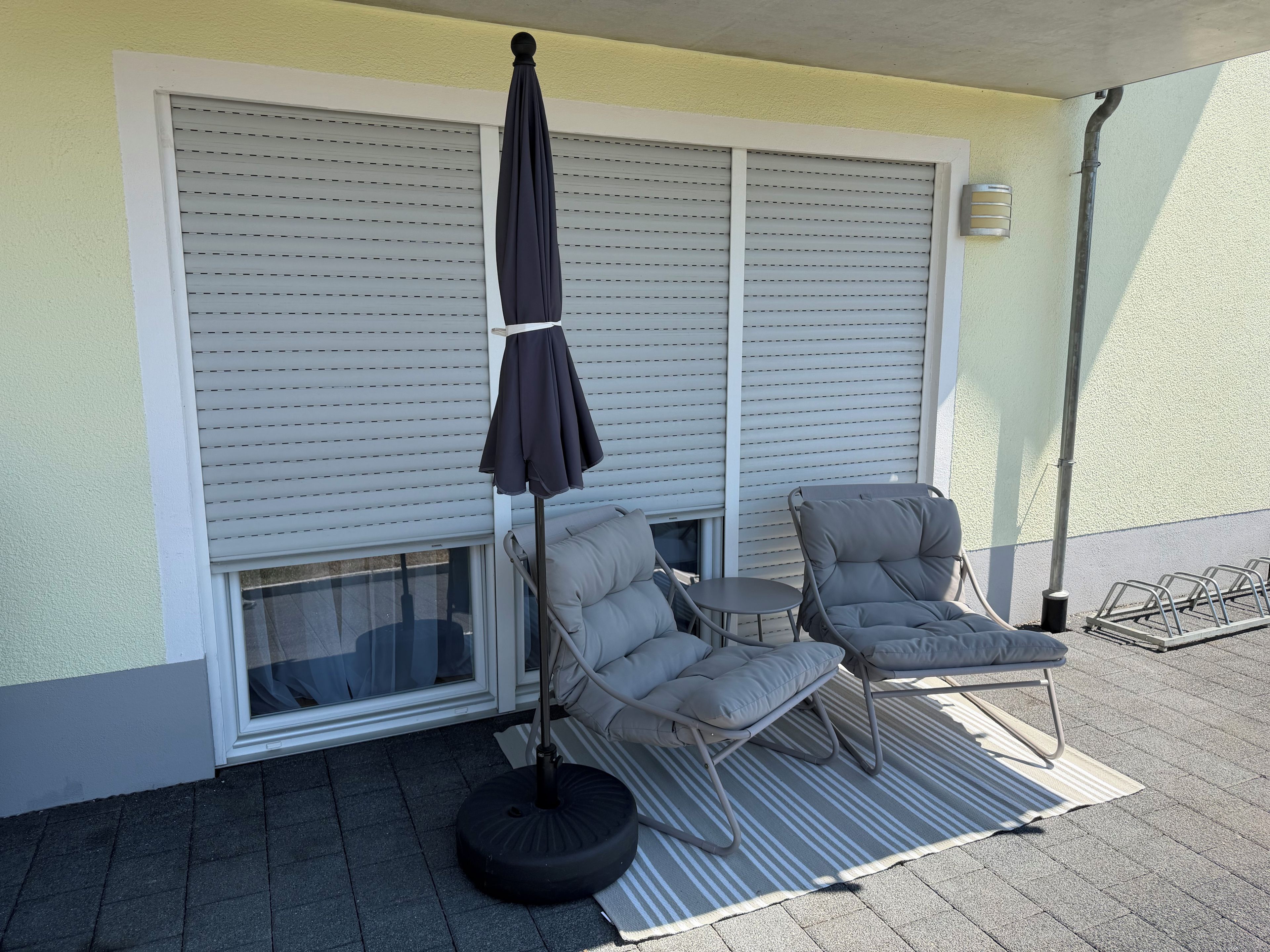 A patio with two chairs and a table, an umbrella, and a window with blinds.