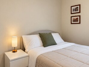 A neatly made bed with a white and green pillow, a bedside lamp, and two framed pictures on the wall.