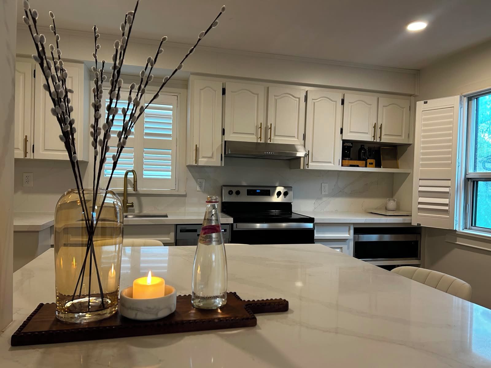 A kitchen with white cabinets, a central island with a candle, and decorative branches.
