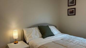 A single bed with white bedding and a green pillow, a bedside table with a lamp, and two framed pictures on the wall.
