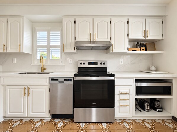 A modern kitchen with white cabinetry, stainless steel appliances, and a patterned tile floor.