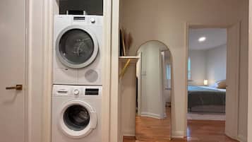 A laundry room with stacked washing machines and a hallway leading to a bedroom.