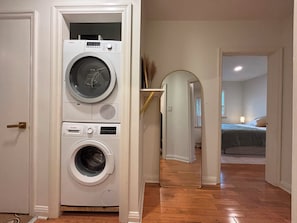 A laundry room with stacked washing machines and a hallway leading to a bedroom. - BRAND NEW 3BR Home | Yorkdale | Roger's Stadium (Toronto)