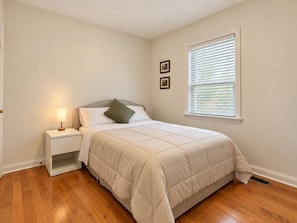 A bedroom with a bed, nightstand, lamp, and window.