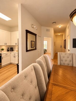 A modern kitchen with white cabinets, a dining area with a wooden table and beige upholstered chairs, and a hallway leading to another room. - Lakeview 3-Bedroom Resort Condo | 15 Minutes from Disney | 4 Pools (Davenport)