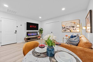 Un soggiorno moderno con zona pranzo, una TV a schermo piatto che mostra 'NETFLIX' e un angolo salotto accogliente.