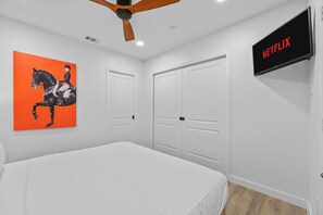 A bedroom with a bed, a ceiling fan, a TV displaying 'NETFLIX', and a painting of a horse. - 2-bedroom Duo apartment in charming Dallas Bishop Arts Downtown (Dallas)