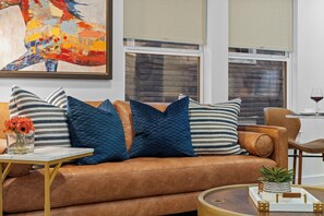 A brown leather sofa with striped and textured pillows, a small table with a vase of flowers, and a glass coffee table with decorative items. - 2-bedroom Duo apartment in charming Dallas Bishop Arts Downtown (Dallas)