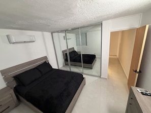 Ein Schlafzimmer mit einem Bett, einem Nachttisch, einem Spiegel und einer Schiebetür zu einem weiteren Raum.