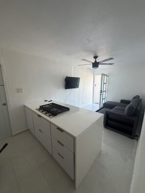 A compact living space with a kitchenette, a flat-screen TV mounted on the wall, a ceiling fan, and a sofa. - 2-bedroom apartment, living room, bathroom, with its own parking space (Toa baja)