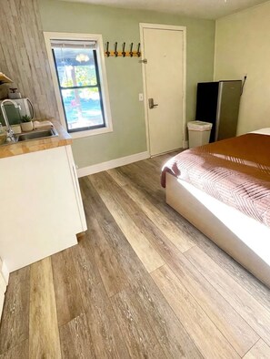 A room with a bed, a window, a door, a sink, and a refrigerator. - Honey Bear Lodge - Unit 1 - Located in the heart of Red River (Red River)