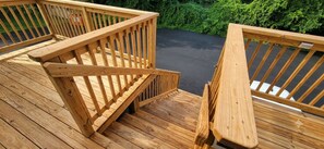 Um deck de madeira com escada que leva a um nível superior, cercado por vegetação.