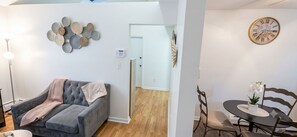 Uma sala de estar moderna com um sofá cinzento, um relógio de parede e um espaço de jantar com mesa e cadeiras.