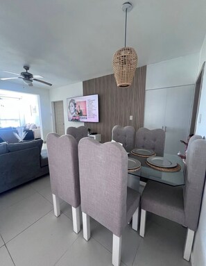 A modern dining area with a glass table, grey upholstered chairs, and a woven pendant light. - Vrbo Property (Punta Cana)