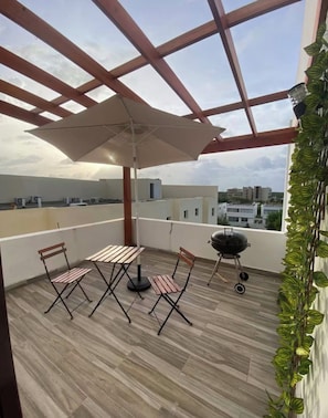 A balcony with a wooden floor, a table with chairs, a grill, and a large umbrella. - Vrbo Property (Punta Cana)