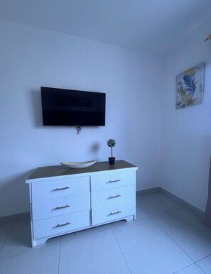 A room with a white dresser, a flat-screen TV mounted on the wall, and a small potted plant. - Vrbo Property (Punta Cana)