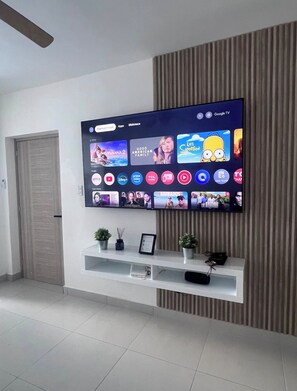 A modern living room with a large flat-screen TV mounted on a wall, a white entertainment unit below, and a closed door to the left. - Vrbo Property (Punta Cana)