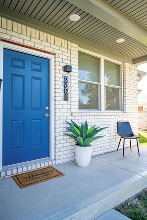 Une maison avec une porte bleue, un pot de fleurs, une chaise et un paillasson.