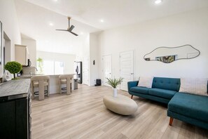 Un salon moderne avec un canapé d’angle, un coin repas doté de tabourets de bar et une cuisine avec un îlot central indépendant.