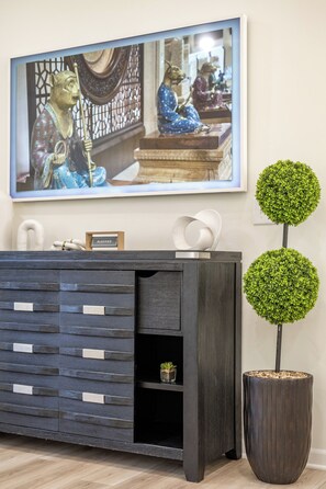 Un intérieur moderne avec une console en bois foncé, une œuvre d’art encadrée au-dessus, et deux plantes vertes en forme de sphère.