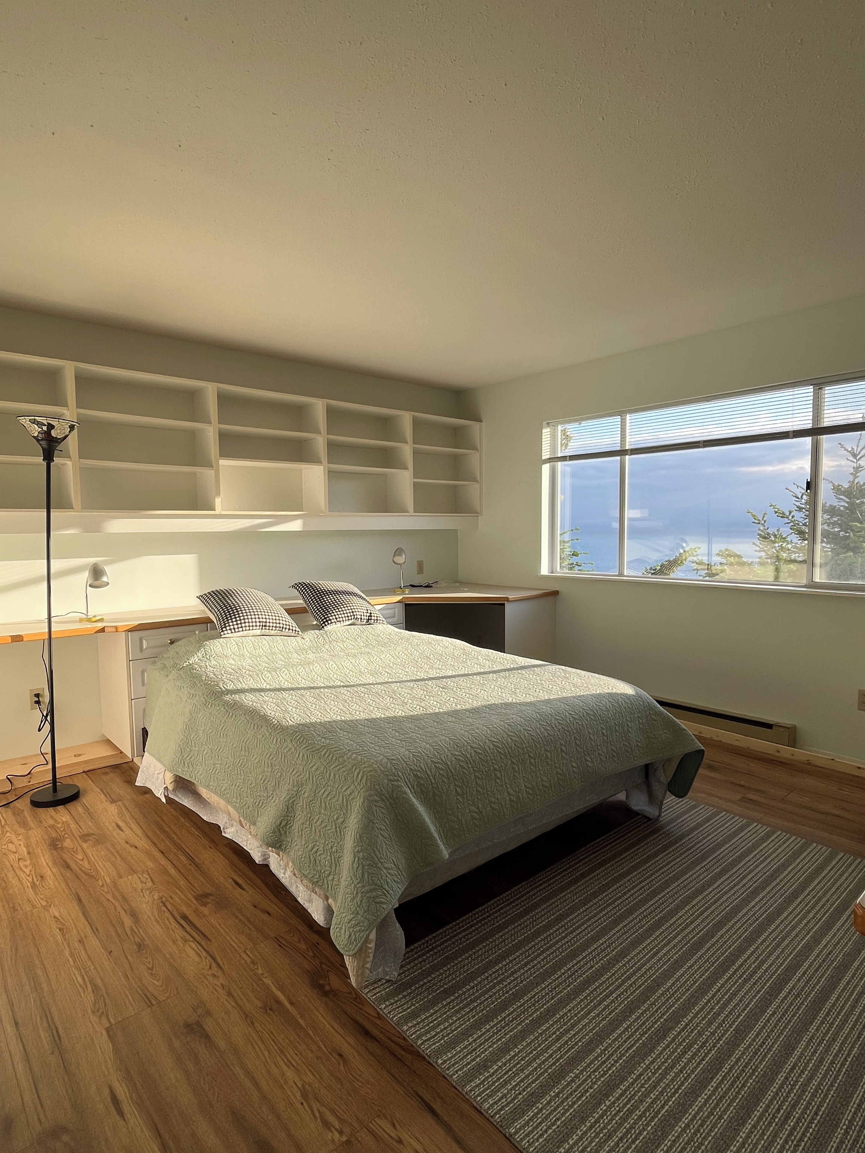 Een slaapkamer met een bed, nachtkastjes, een lamp, een raam met uitzicht en ingebouwde planken.
