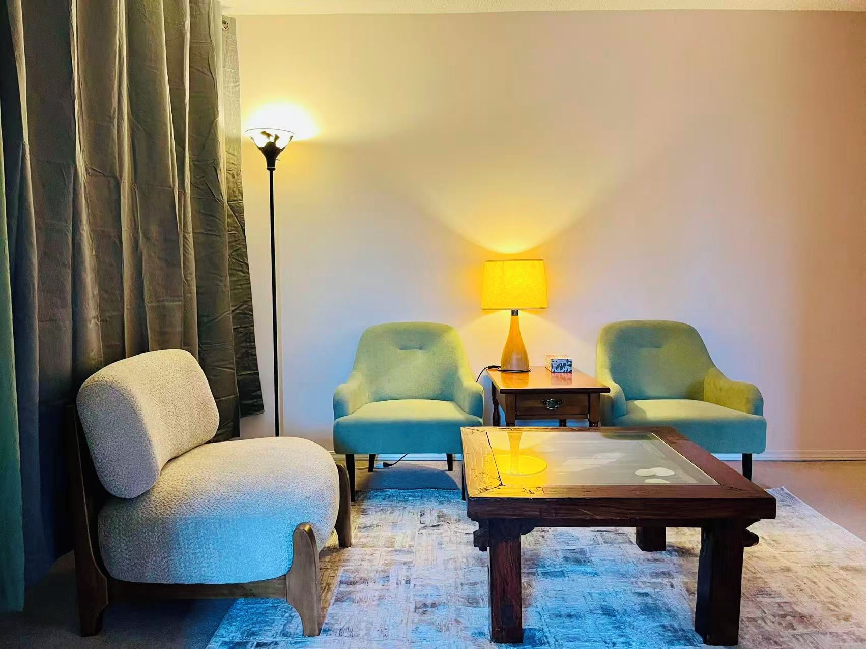 Een kamer met een bank, twee fauteuils, een salontafel, een lamp en een vloerlamp.