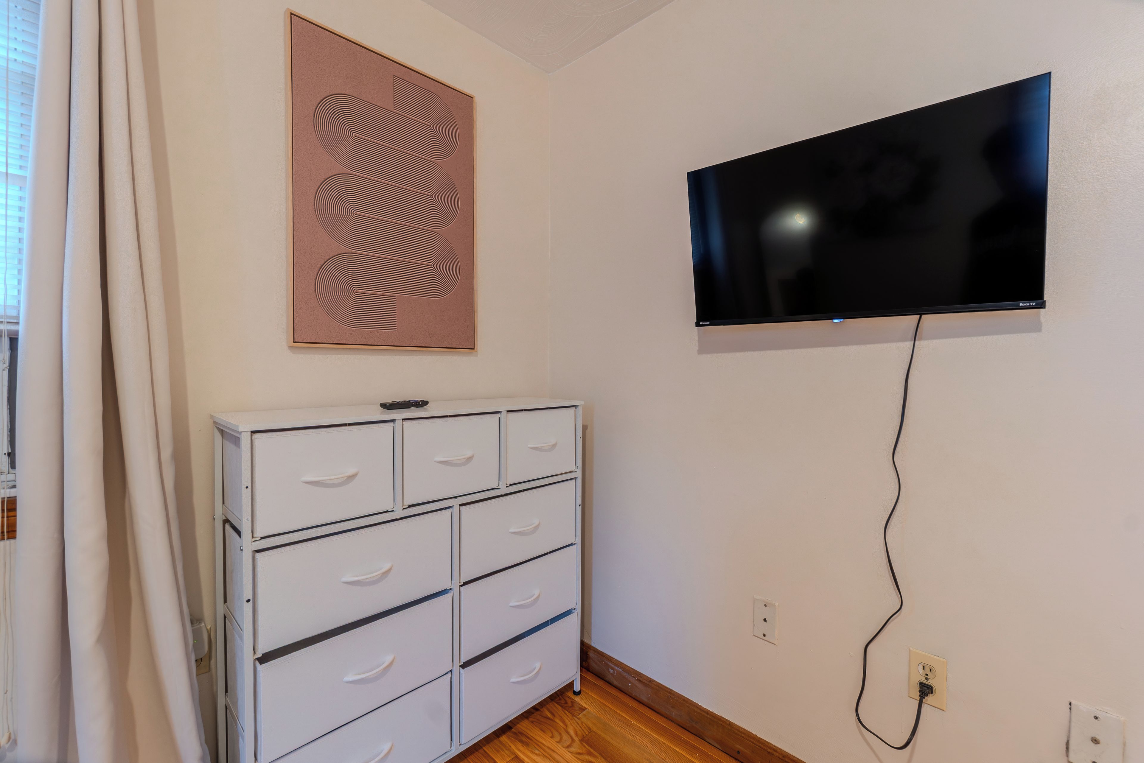 Ein Zimmer mit einem weißen Schminktisch, einem gerahmten Kunstwerk und einem an der Wand befestigten Fernseher.