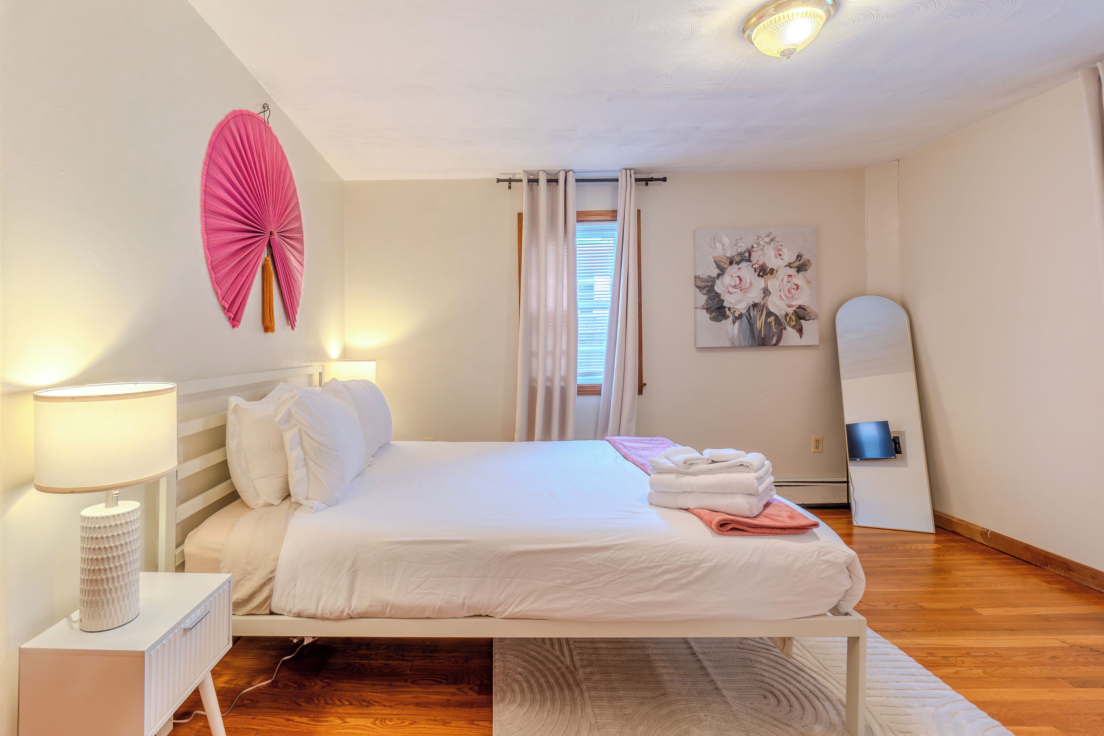 Una cama bien tendida con sábanas blancas, una lámpara de noche y un ventilador decorativo fijado a la pared.