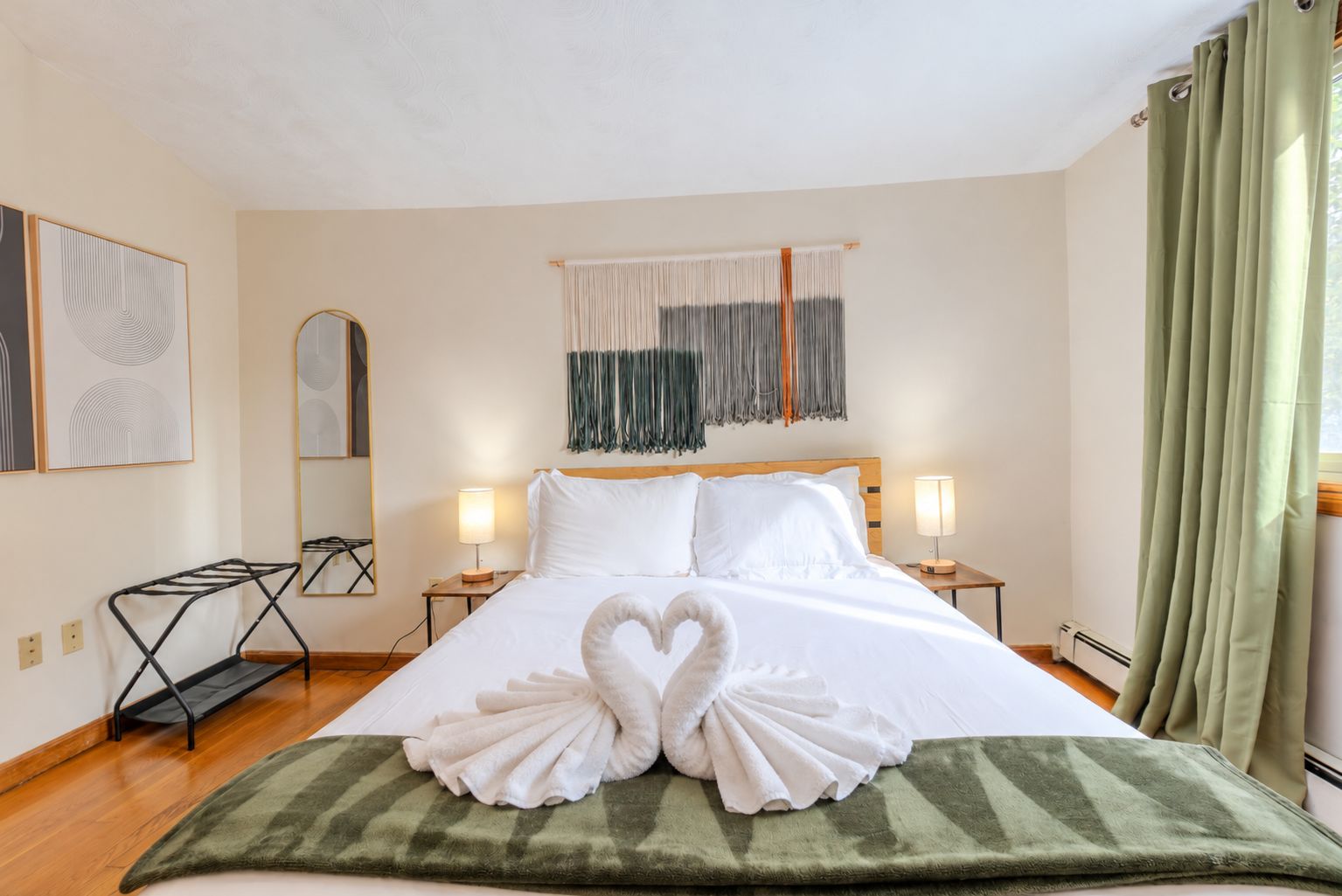 Ein Hotelzimmer mit einem ordentlich bezogenen Bett, zwei Nachttischlampen, einem Spiegel und einer grünen Tagesdecke.