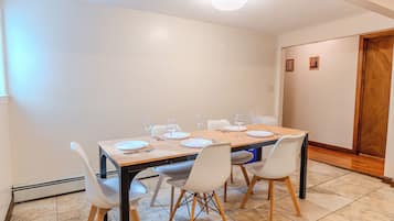 Ein Essbereich mit einem rechteckigen Tisch, gedeckt für vier Personen, umgeben von weißen Stühlen mit Holzbeinen.