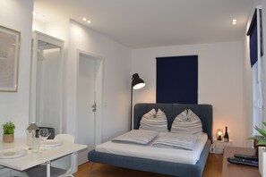 Et soveværelse med seng, natbord, lampe og et lille bord med flaske og glas.