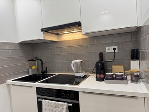 Et moderne køkken med indbygget komfur, kaffemaskine og elkedel på bordpladen.